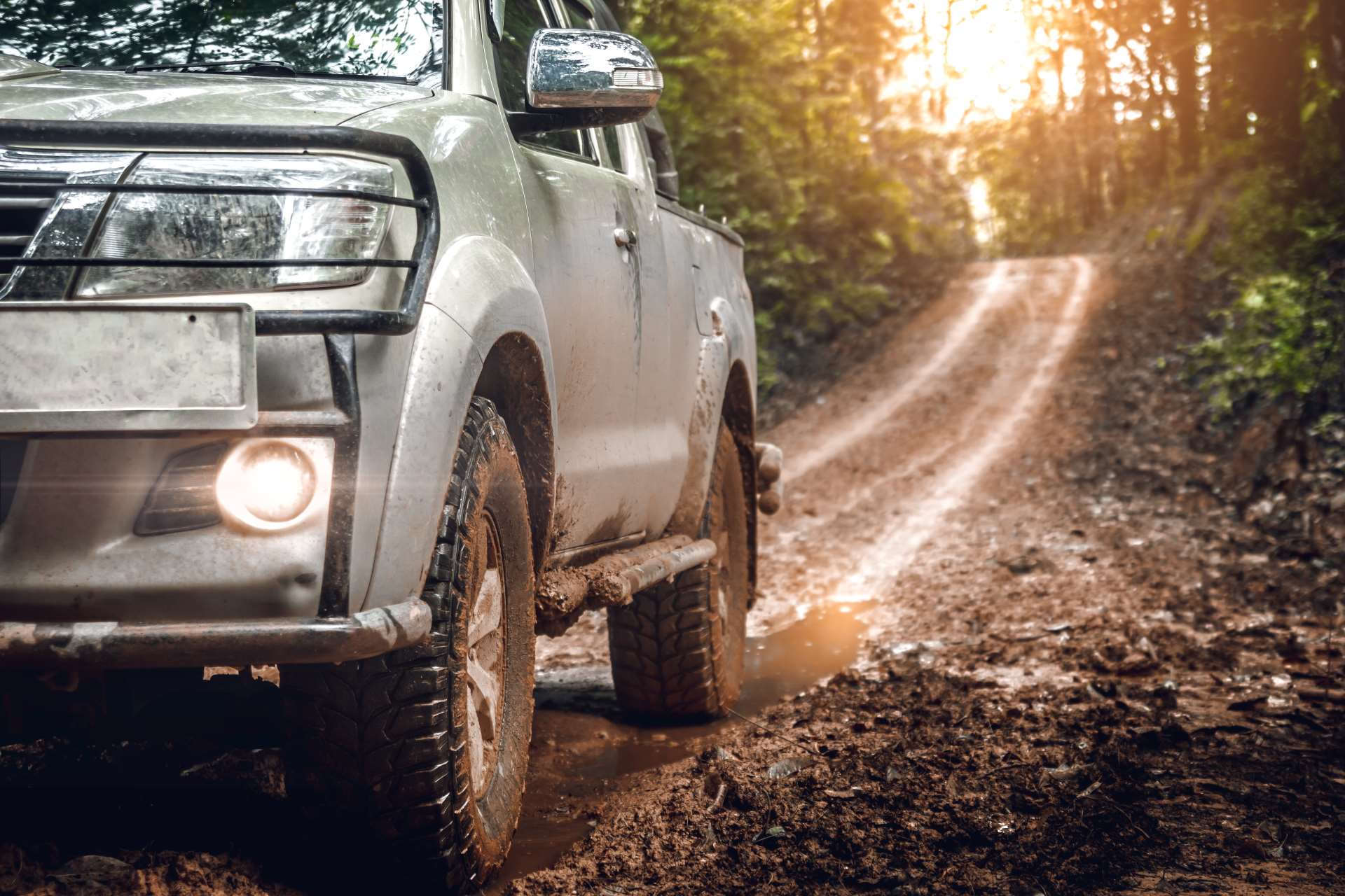 A modified gray truck off-roading in mud featuring a headlamp grill and a modified step bar for convenient entry