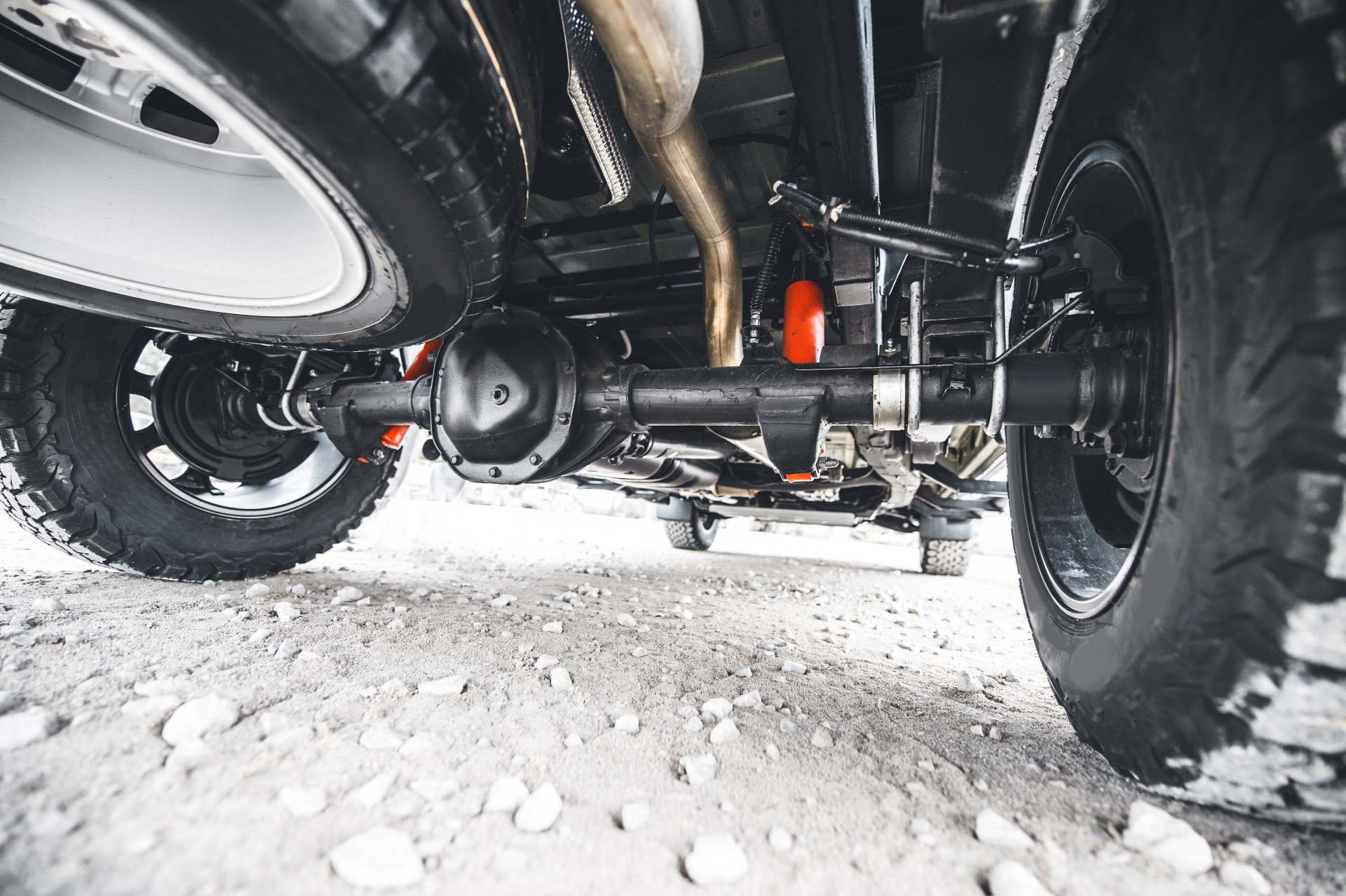 POV of a truck owner under a truck inspecting the axle, suspension and exhaust systems under the chassis