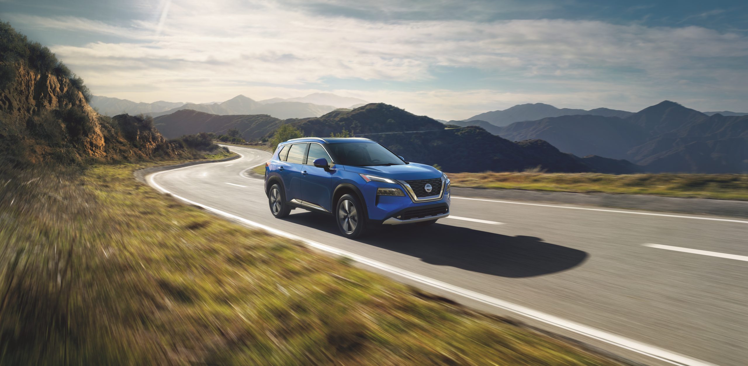 Blue Nissan Rogue driving down a winding road in a mountain area