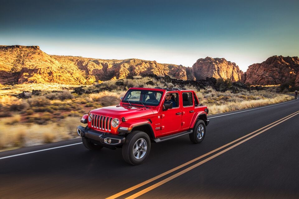 Red Jeep Wrangler driving down an open road in the desert