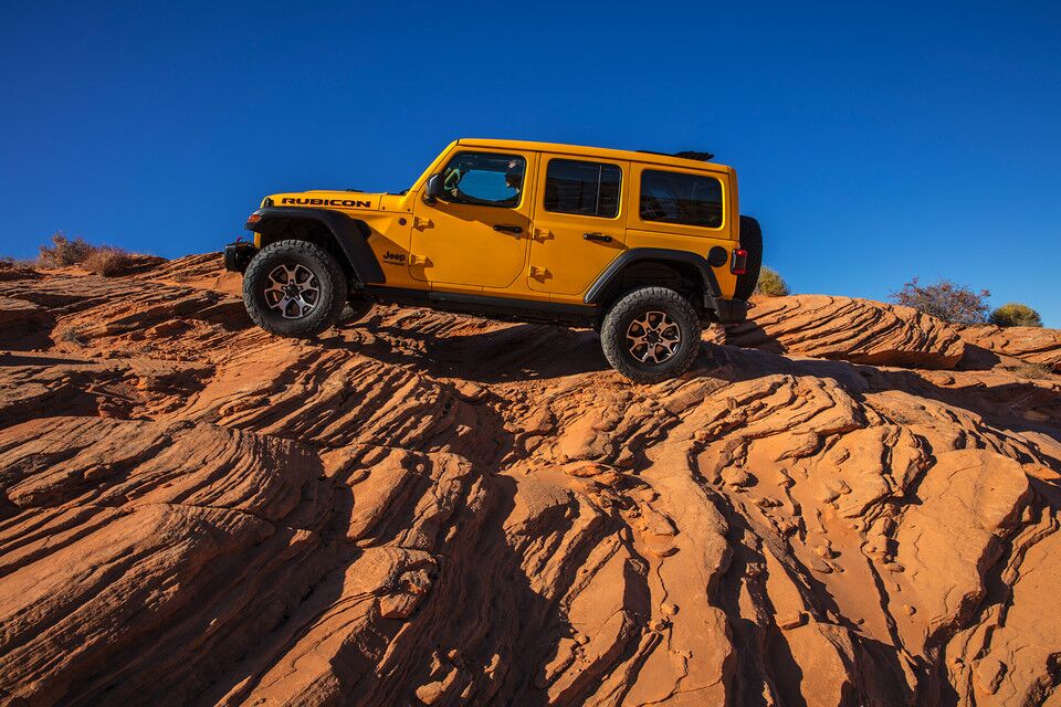 Yellow Jeep Wrangler showcasing capabilities parked on the side of a mountain in a desert setting