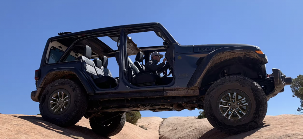 Passenger side view of a Jeep Wrangler with no doors driving over rocks in the desert