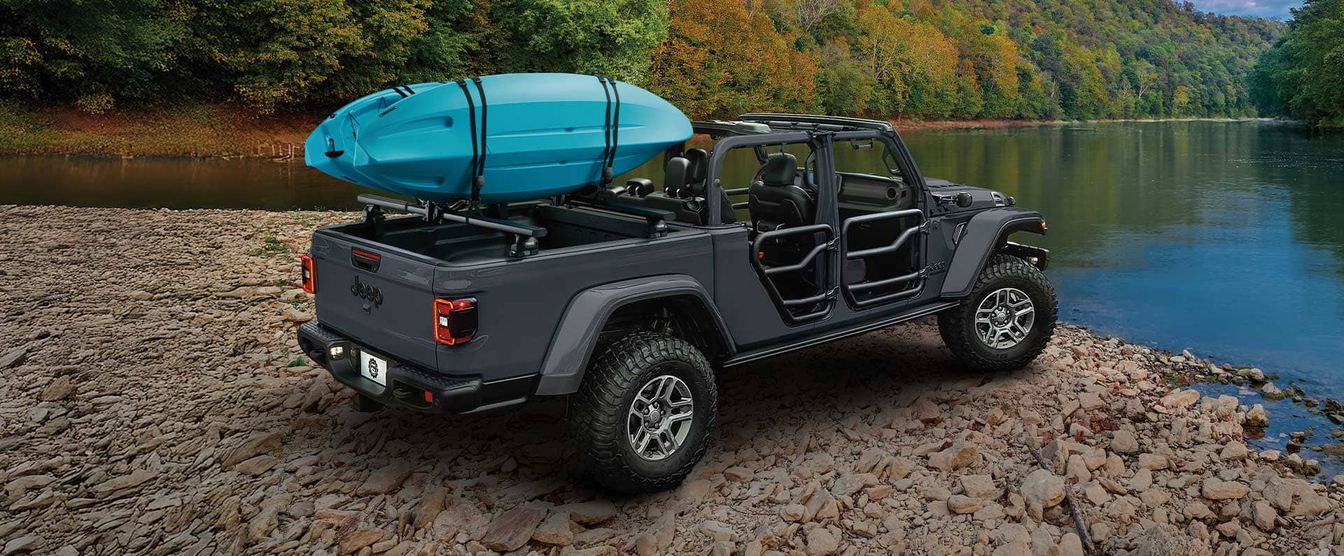 2026 Jeep Gladiator with kayak mounted on cargo bed rack parked by a river