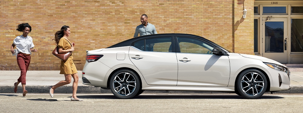 A trio of people preparing to get into a white Nissan Sentra parked by the curb.