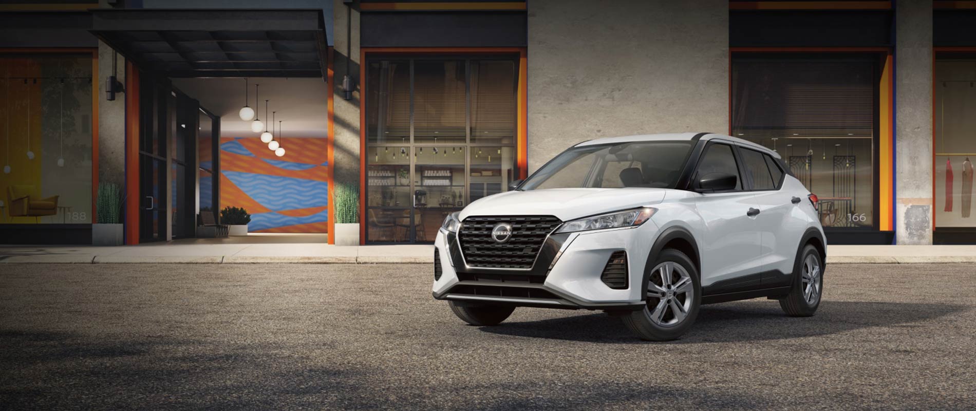 A white Nissan Kicks parked in front of a building in a town.
