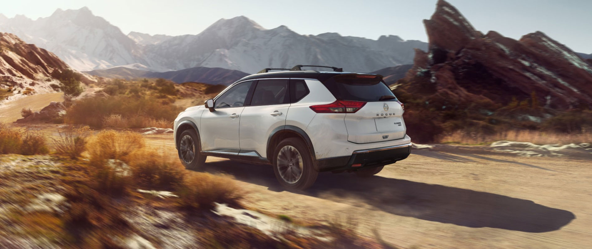 A white Nissan Rogue driving through a rocky desert on a dirt road.