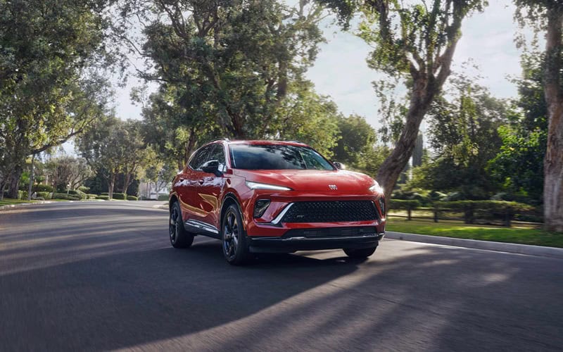 2026 Buick Envision ST in red driving down a tree-lined street