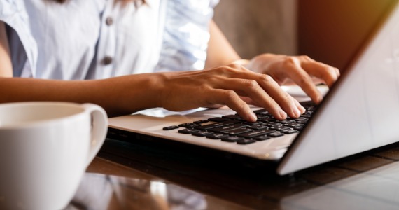 Person typing on a laptop next to a cup of coffee to start the buying process