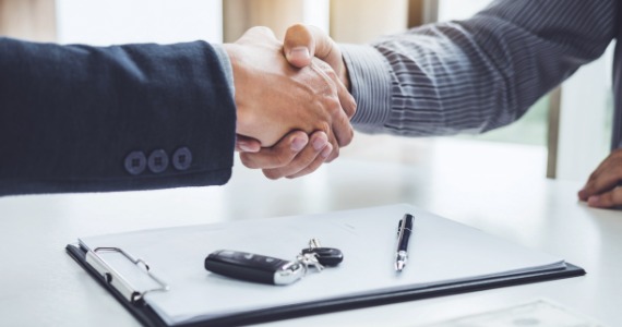 Two people shaking hands over a desk with car keys and paperwork