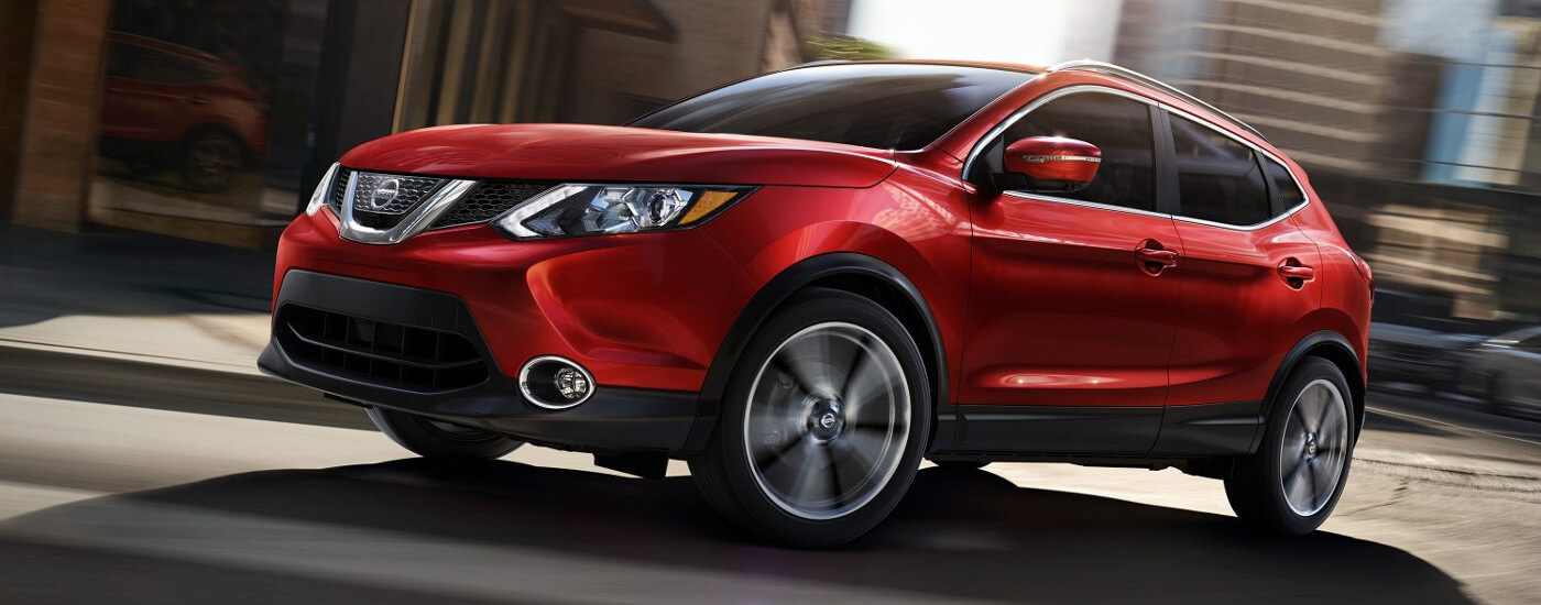 A Red Nissan Rogue Driving Down The Road