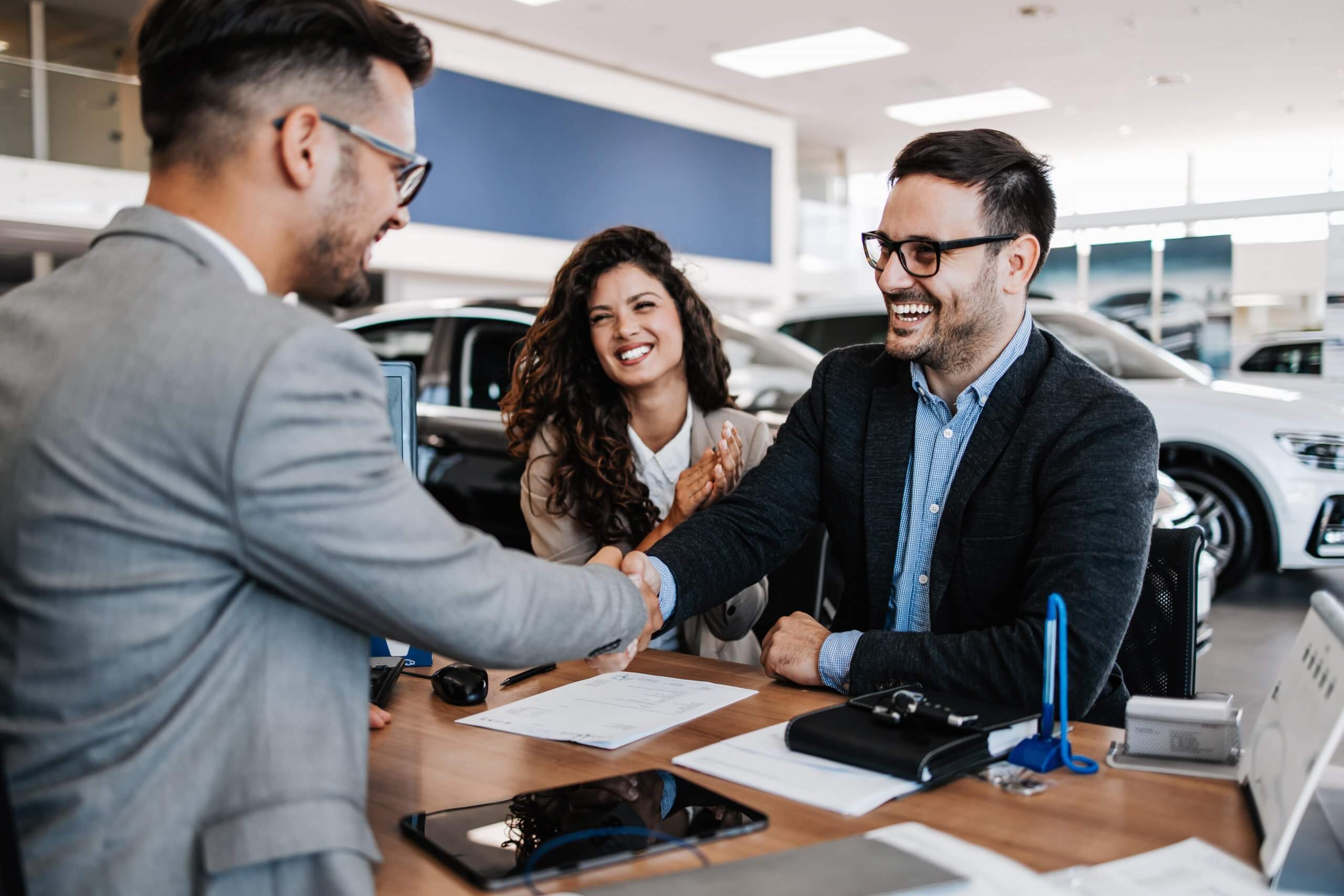 Customers buying a new car and smiling while shaking hands