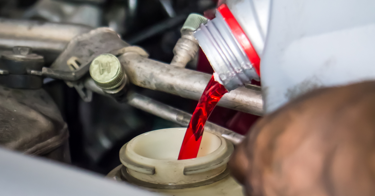 A hand pouring transmission fluid in a car engine