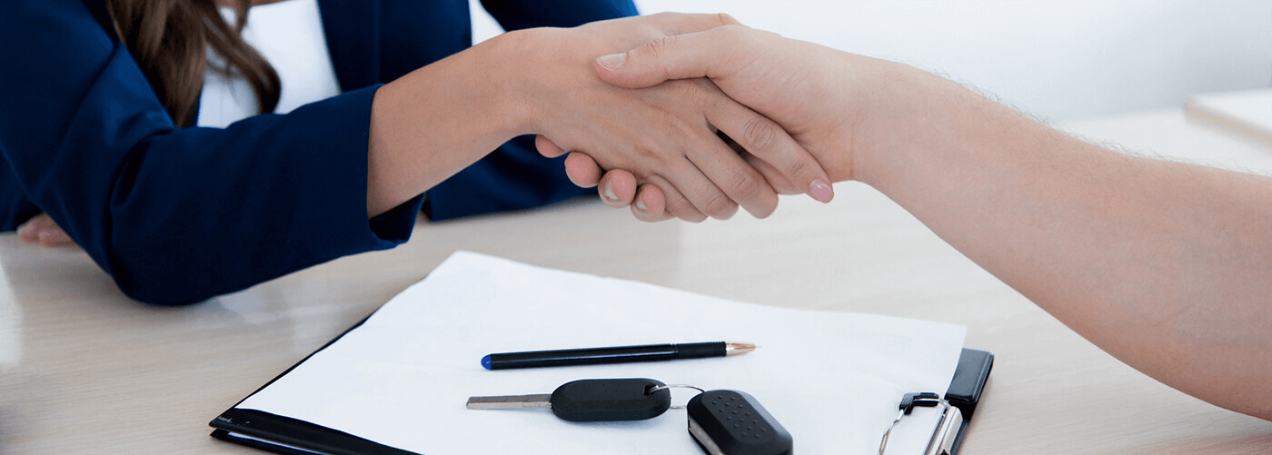 Woman shaking mans hand over a car contract clipboard with car keys 