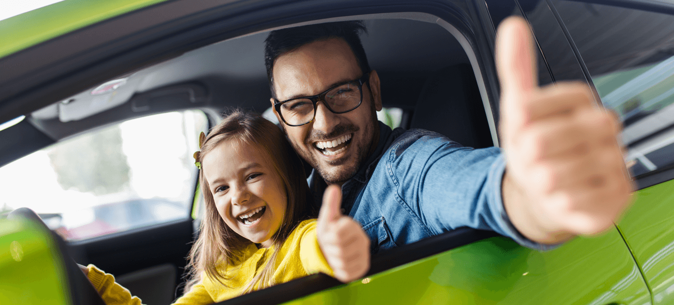 Father and daughther sitting in their new green car.