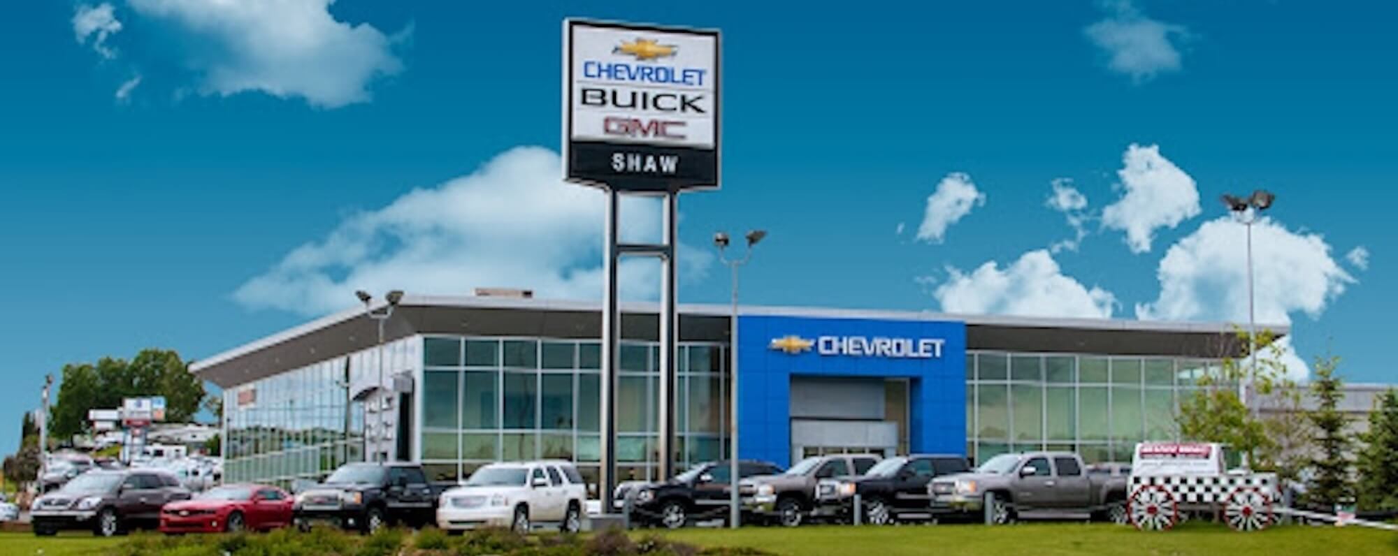 Shaw GMC Chevrolet Buick exterior photo showcasing signage, building, GM trucks, a chuckwagon and other property on a summer day