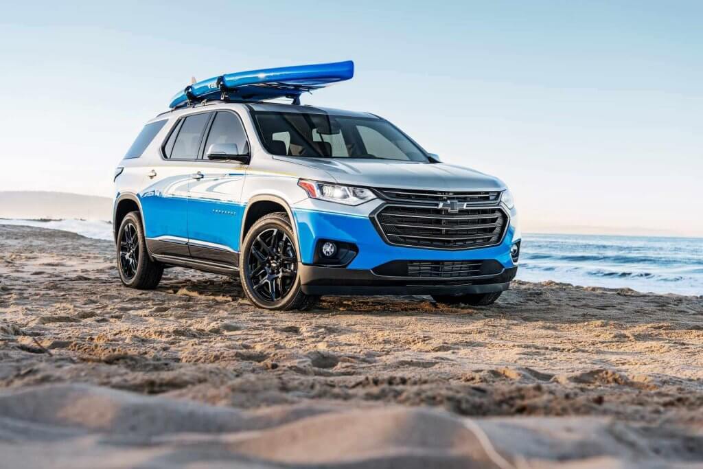 Chevrolet Traverse in upper trim with inflatable stand up paddle board on roof rack off-roading beside water.