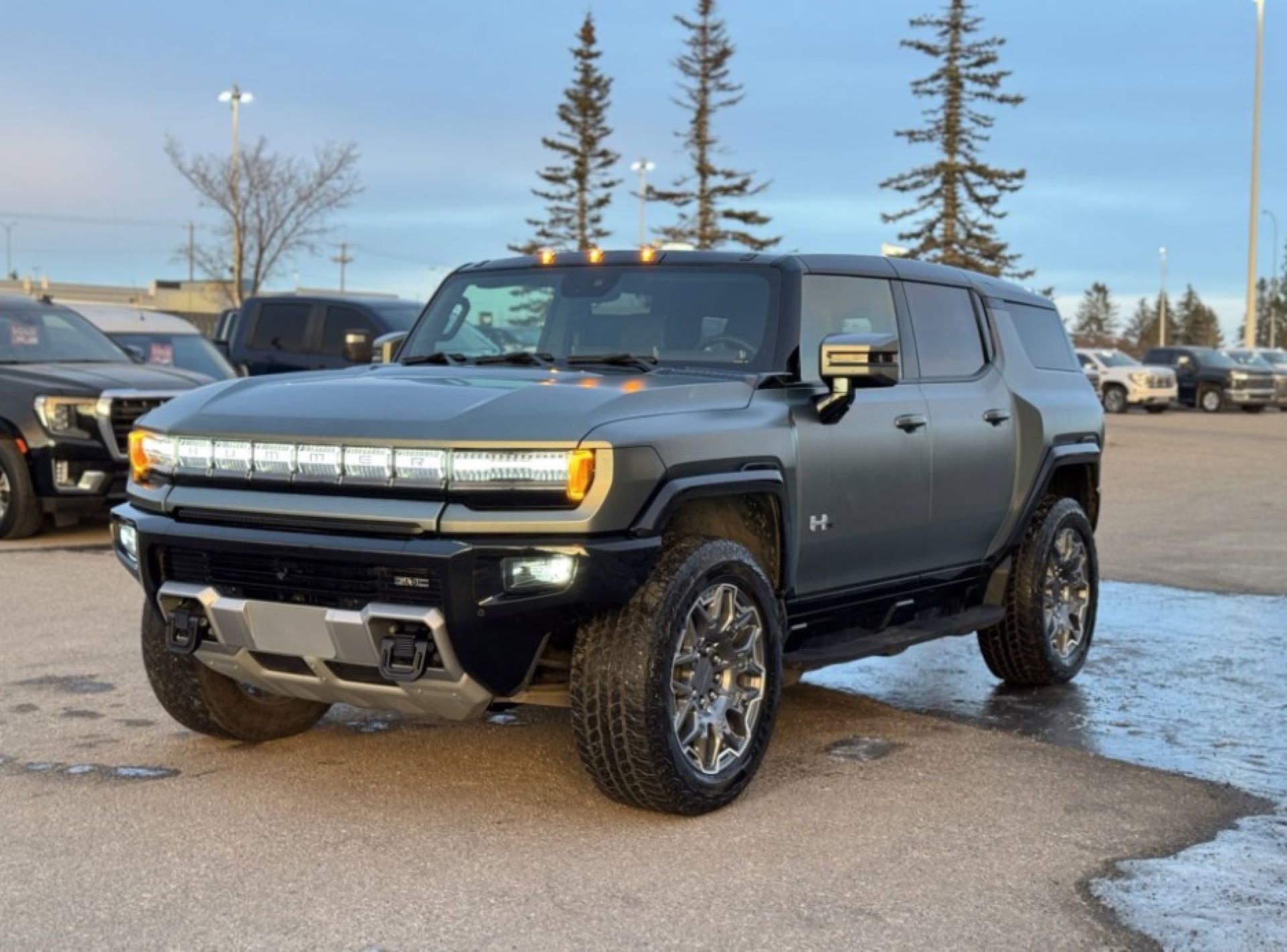 a dark grey hummer ev suv sitting in a parking lot with black ice at sunset