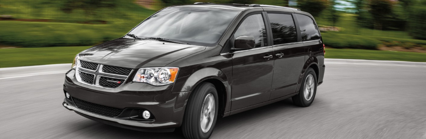 2020 Dodge Grand Caravan winnipeg mb exterior shot with dark black gray paint color driving down a suburban road near bushes and trees