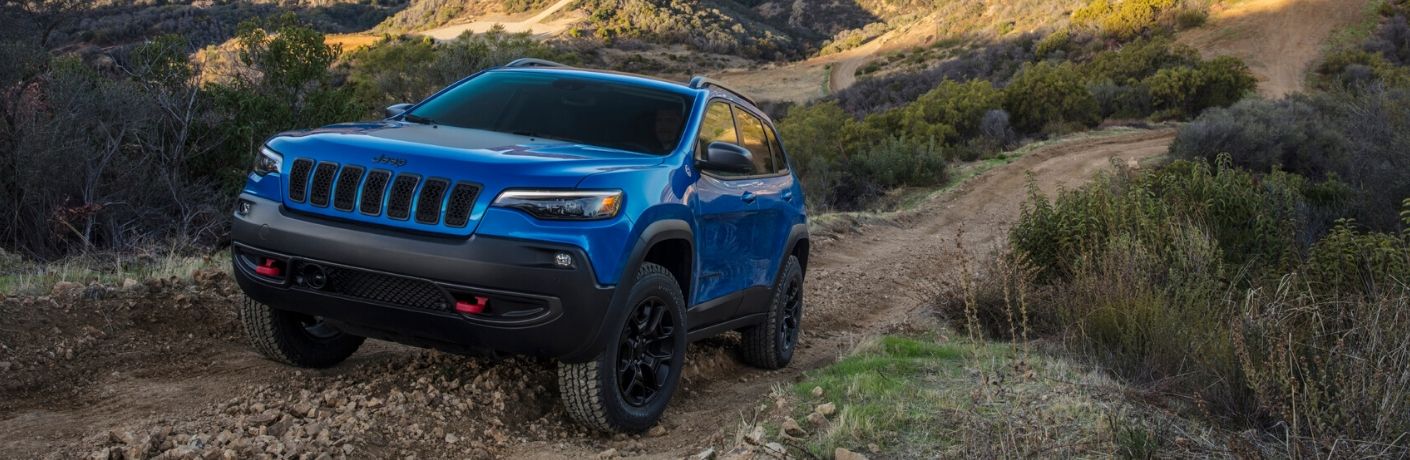 2020 Jeep Cherokee winnipeg mb exterior shot with deep blue color driving up a dirt road on a green hill