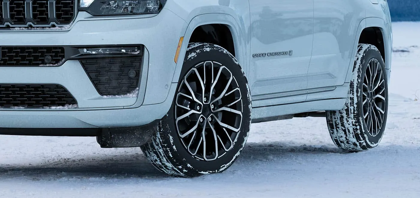Snow-dusted Jeep Grand Cherokee front wheel and door badge on a winter day