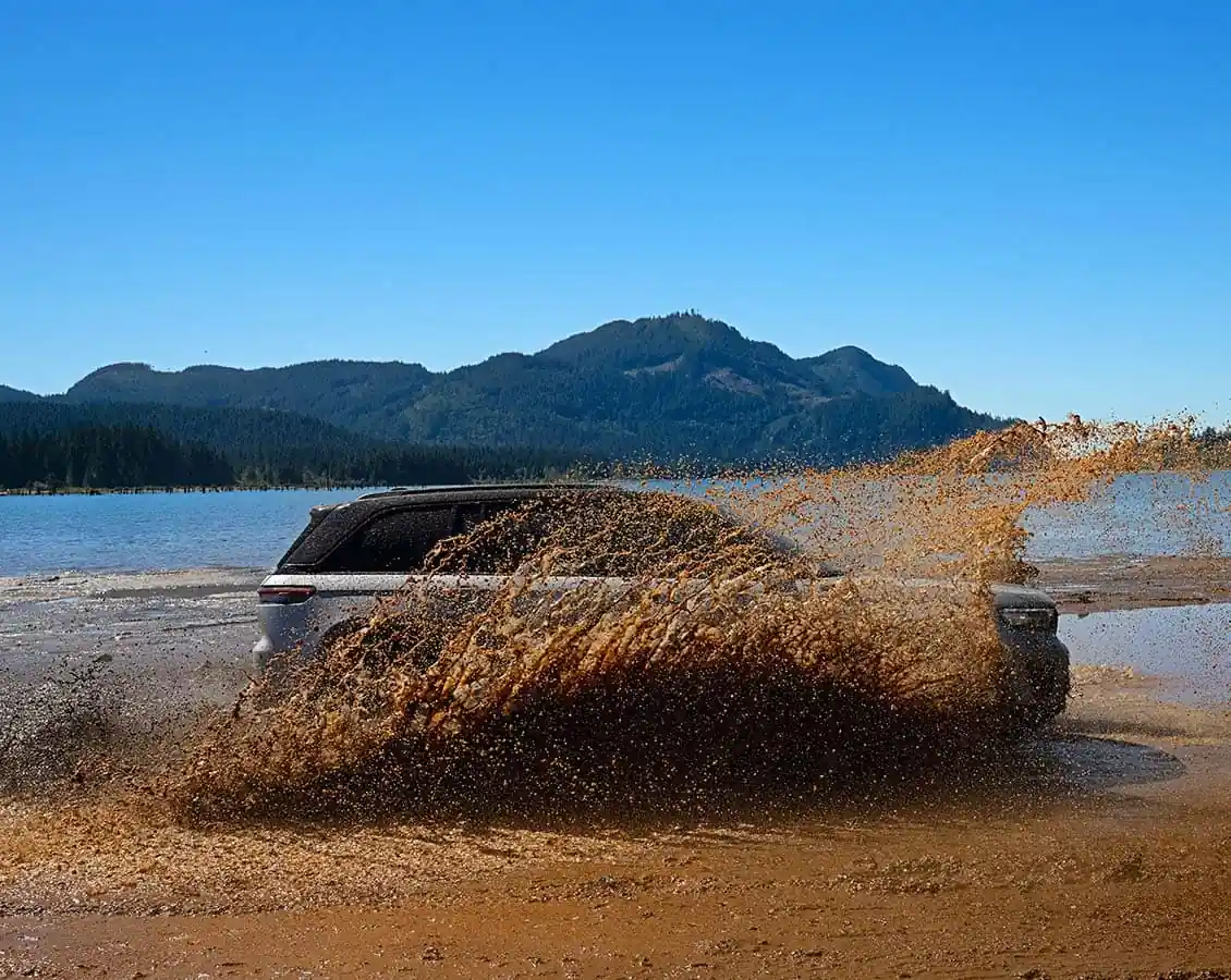 Jeep Grand Cherokee fording water and mud by a lake, spray flying