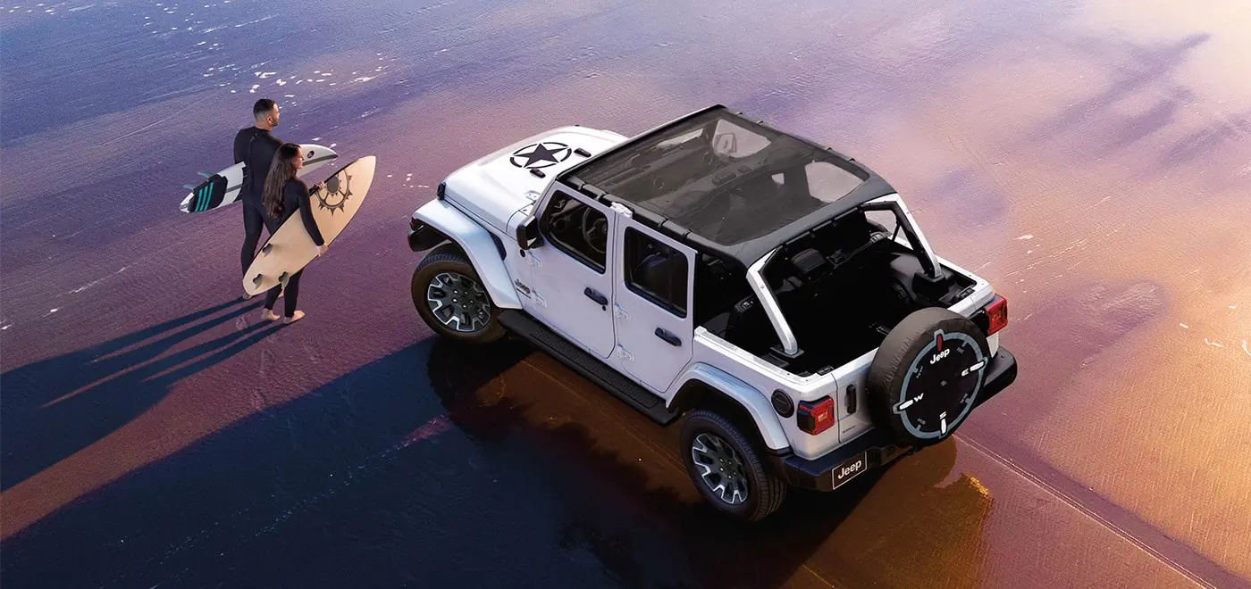 White Jeep Wrangler with the roof open parked on a wet beach at sunset