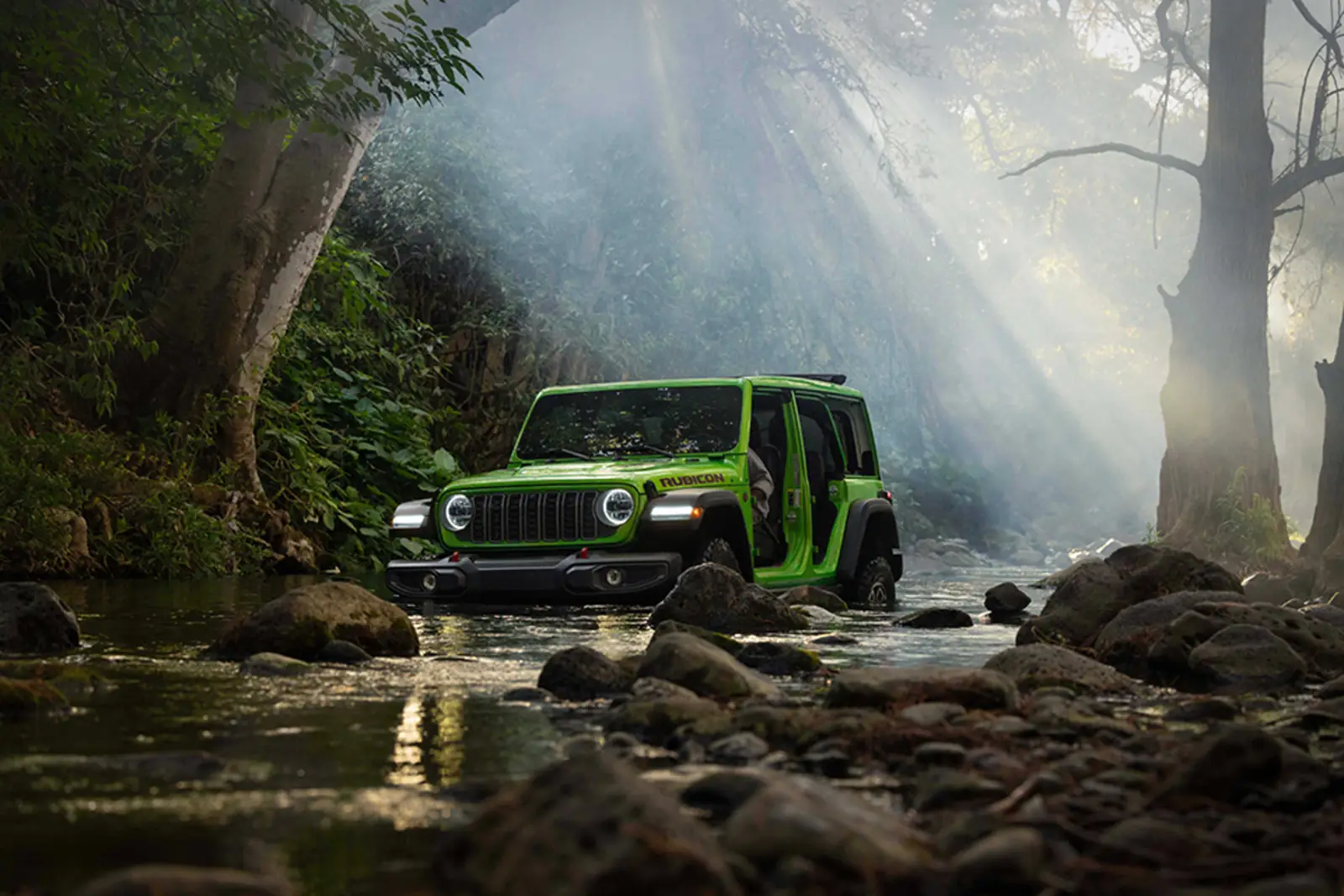 green Jeep Wrangler splashing through water on a forest trail
