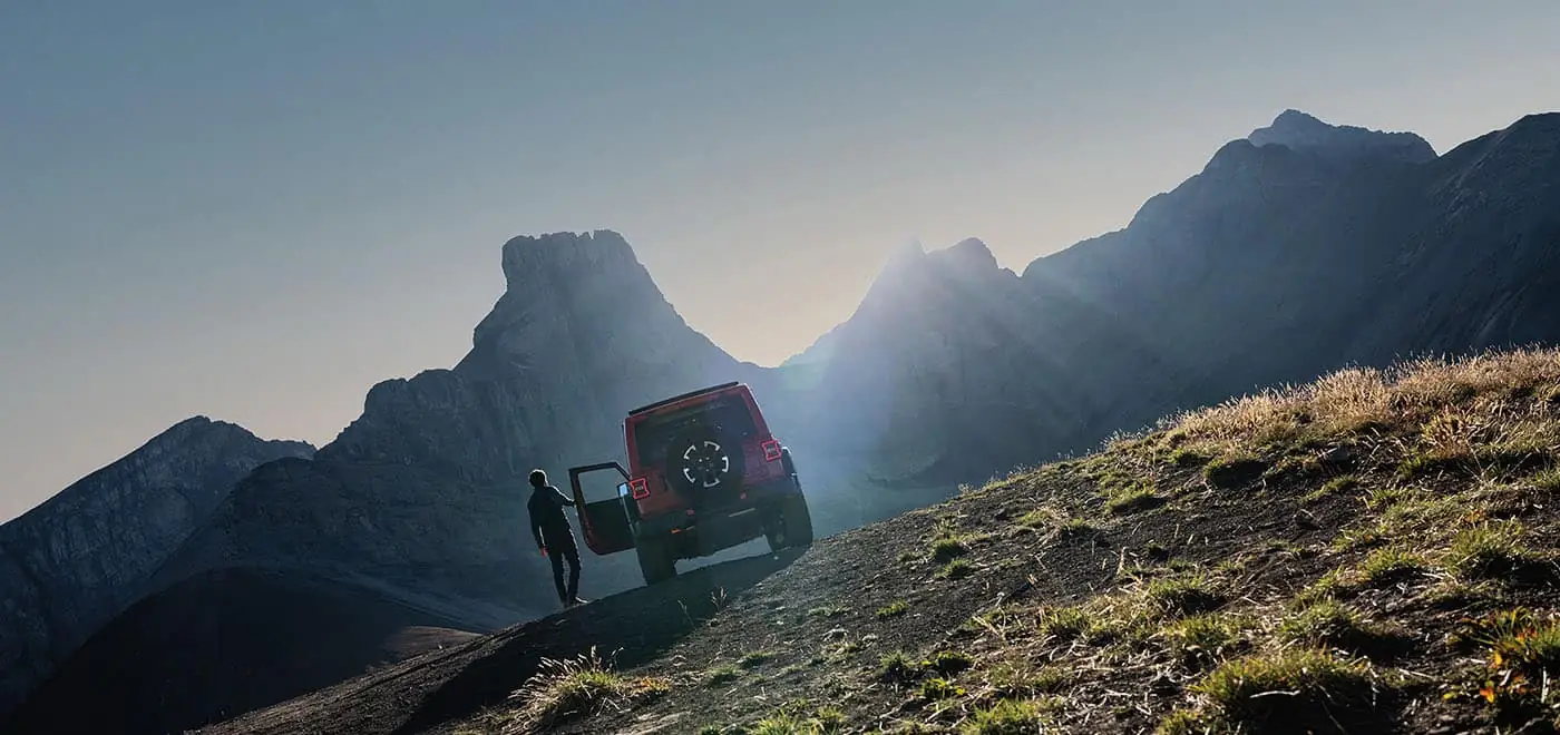 red Jeep Wrangler rear three quarter view on a mountain ridge at sunrise