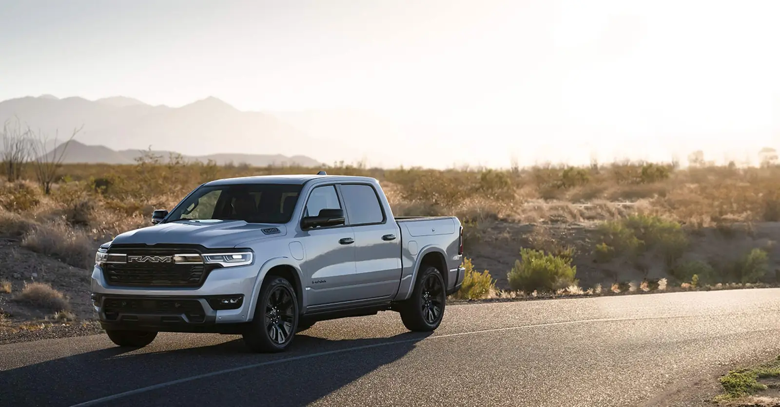 silver Ram 1500 REV on a desert road at dusk with the charge port visible