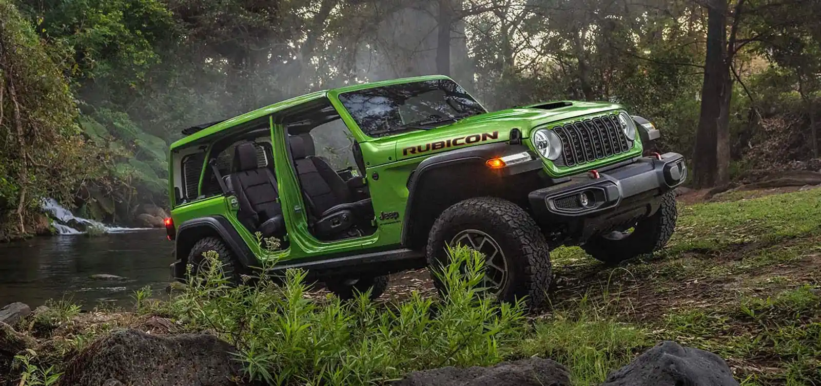 bright green 2026 Jeep Wrangler Rubicon four door with doors off beside a forest creek