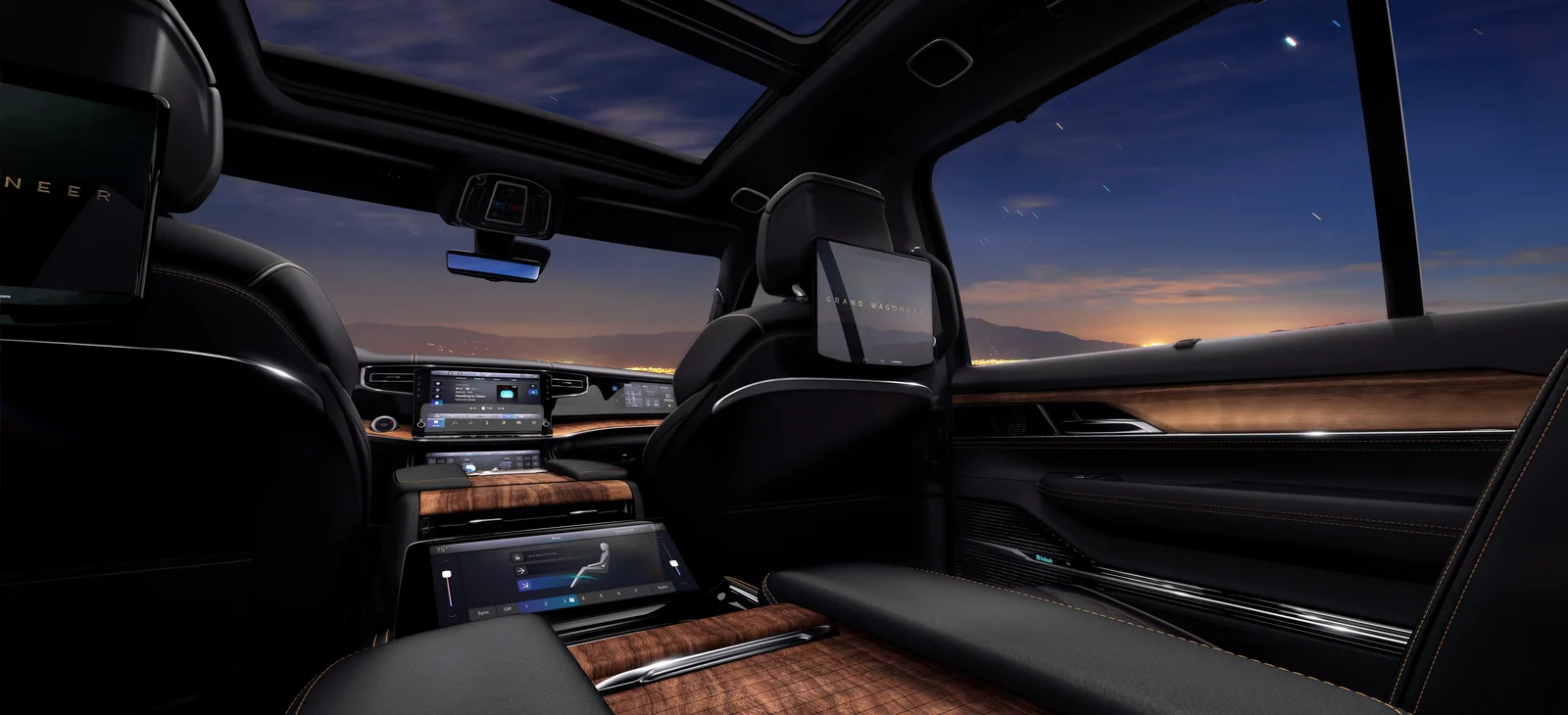 Jeep Grand Wagoneer interior with panoramic sunroof, seatback screens and wood trim at dusk