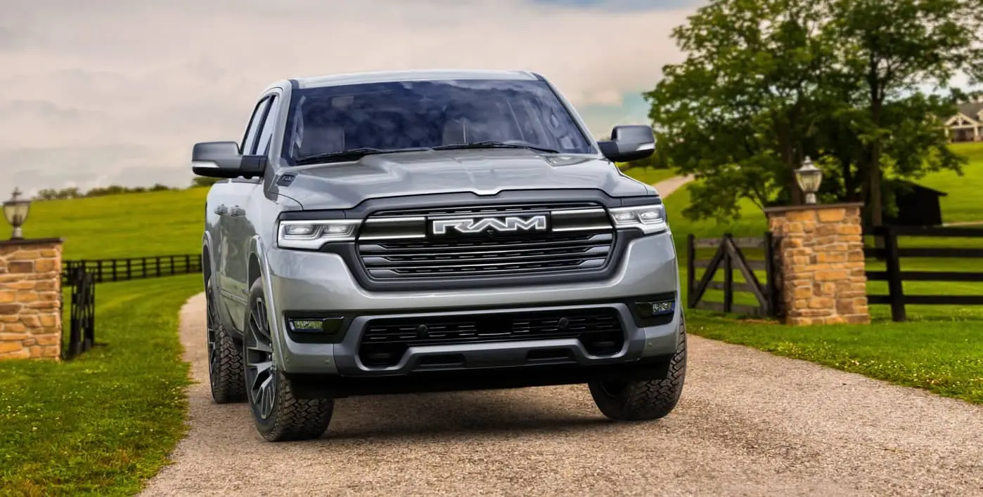 grey 2027 Ram 1500 REV straight on front view on a residential driveway with an illuminated closed grille