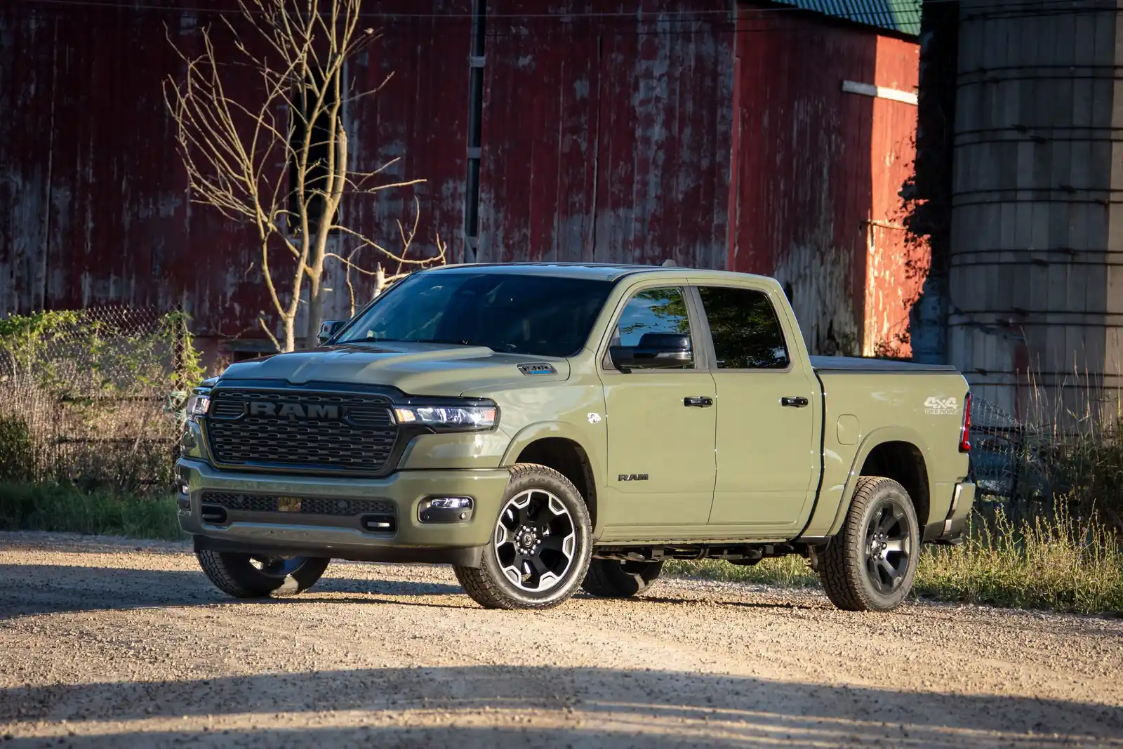 green 2026 Ram 1500 crew cab parked on gravel beside a weathered red barn