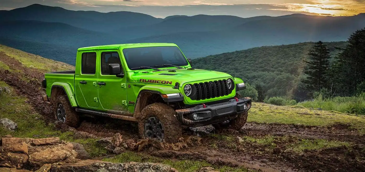 green Jeep Gladiator Rubicon climbing a muddy trail with mountains behind