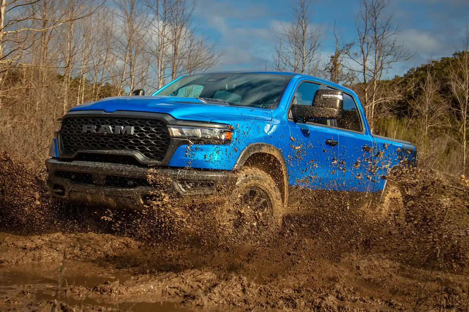 blue 2026 Ram 1500 driving off road through mud