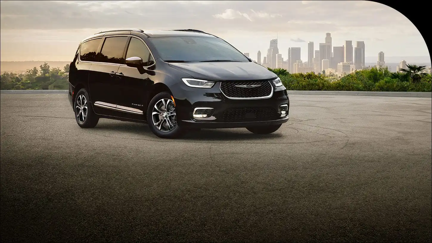 2026 Chrysler Pacifica Pinnacle in black shown front three quarter with a city skyline behind