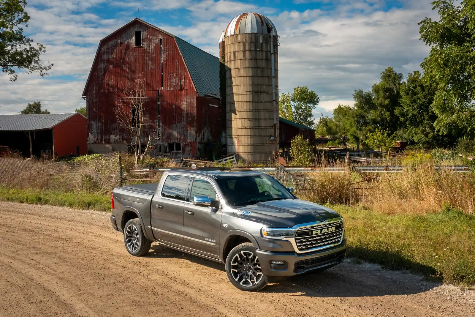grey Ram 1500 Limited crew cab on a gravel farm drive with a red barn behind