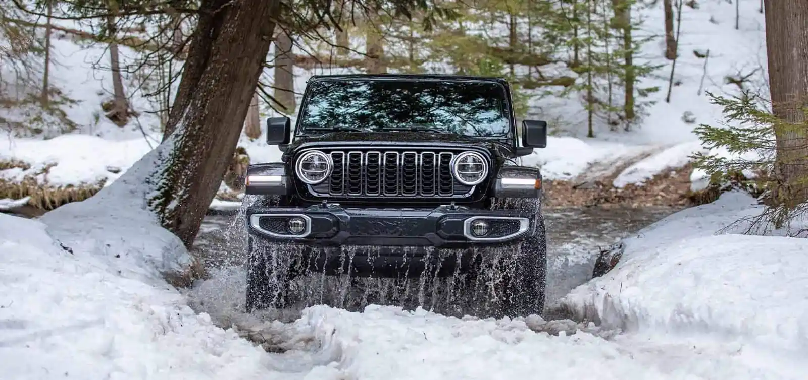 Black Jeep Wrangler fording a snowy forest creek between snow banks