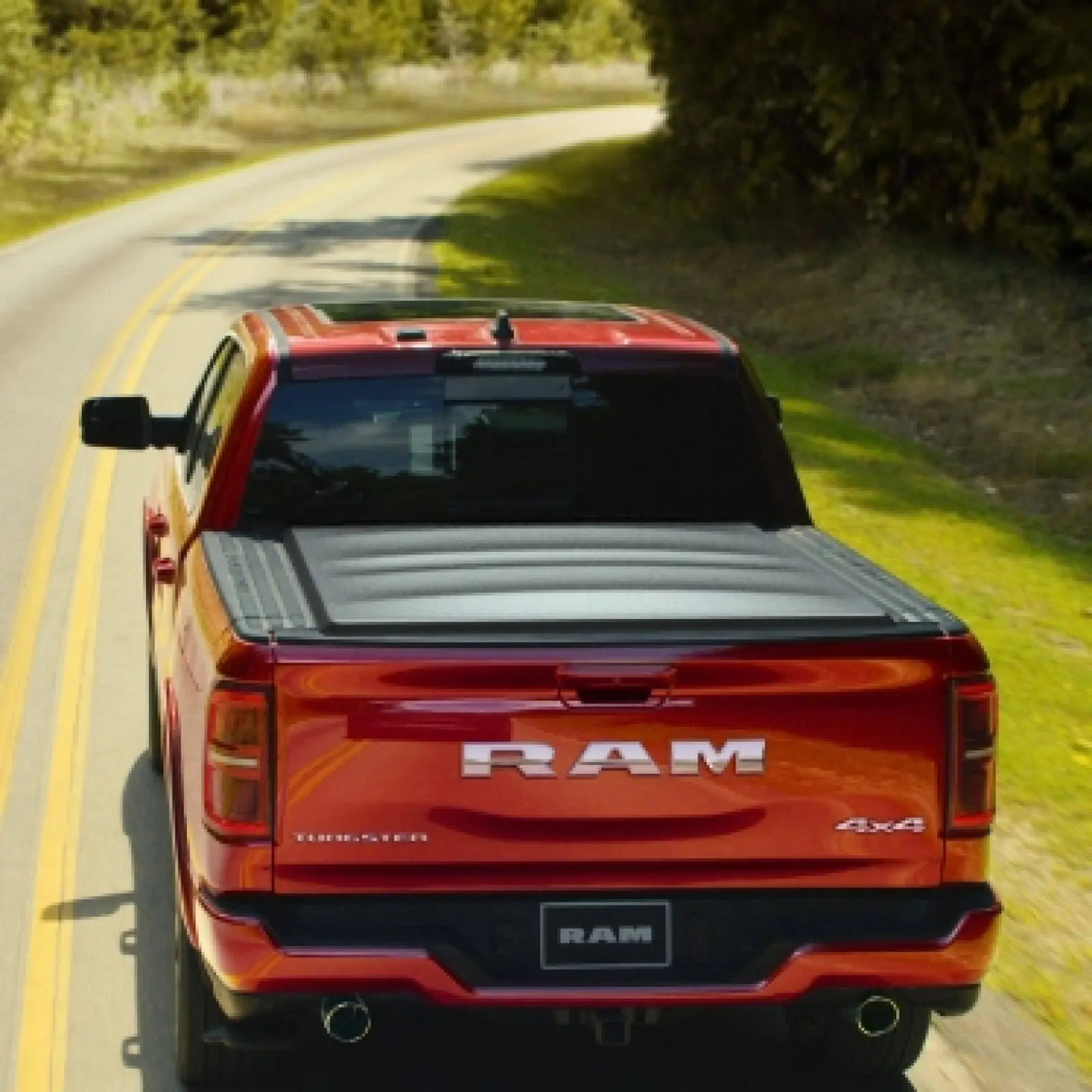 Red Ram 1500 Tungsten crew cab seen from behind on a treelined country road