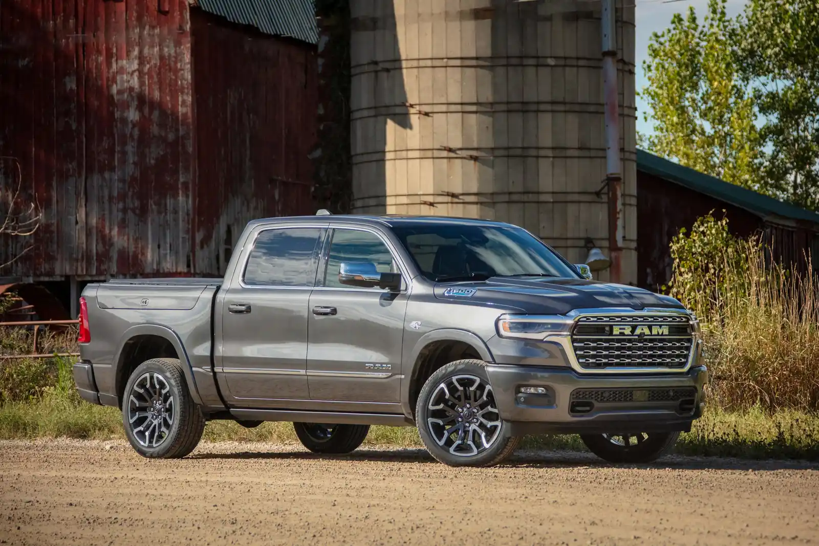 Grey Ram 1500 Limited crew cab on a gravel farm drive beside a red barn and grain silo