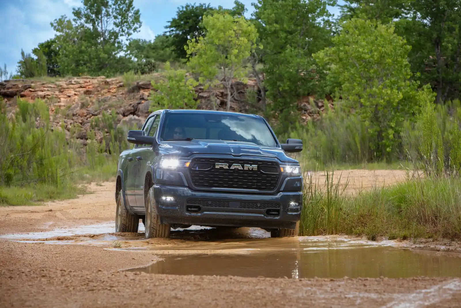 Dark grey 2026 Ram 1500 wading a muddy water crossing on a back road
