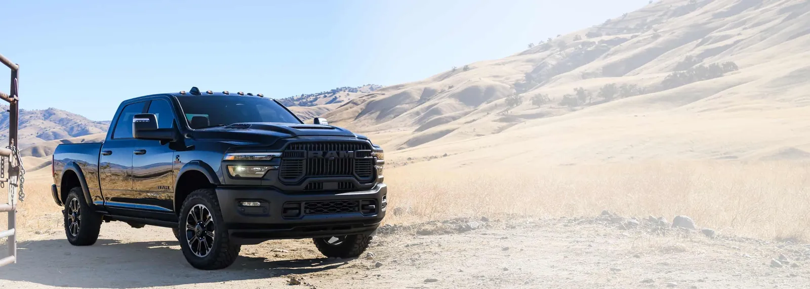 Black Ram 2500 with a Cummins badge parked on a dirt track beside a steel gate