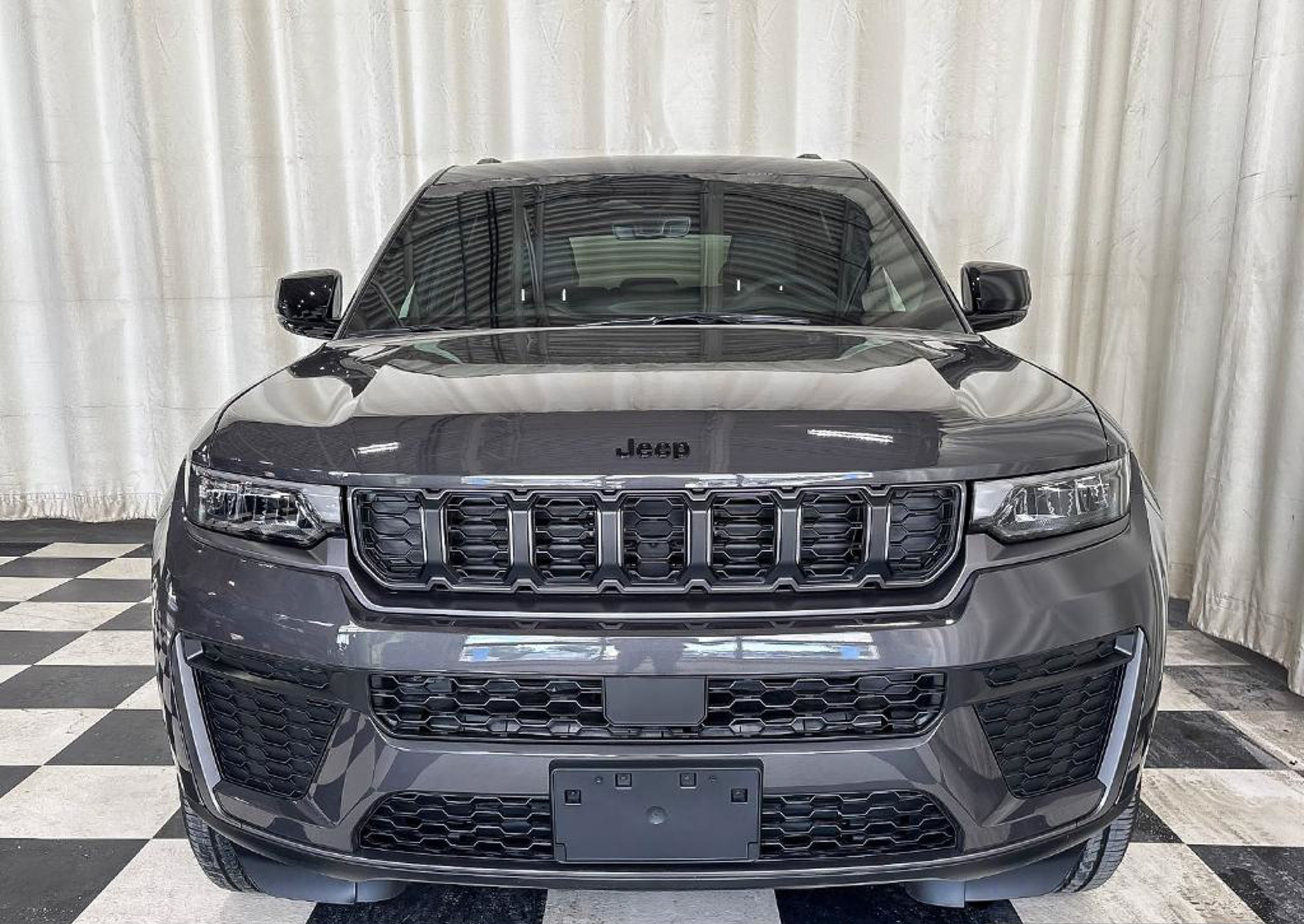 Grey 2026 Jeep Grand Cherokee Altitude with its dark grille seen head on in a dealership photo studio