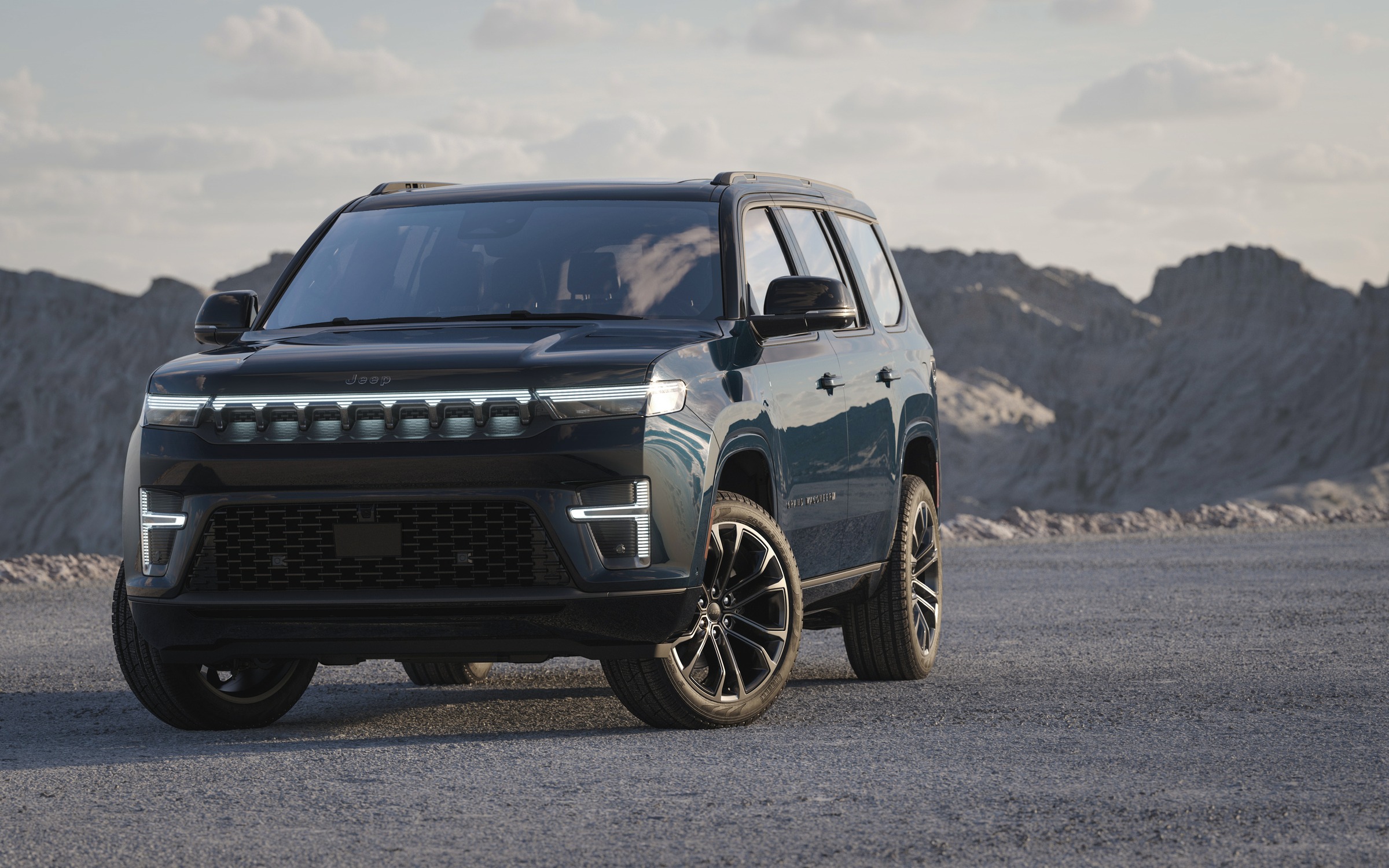 dark teal Jeep Grand Wagoneer parked on gravel with mountains behind