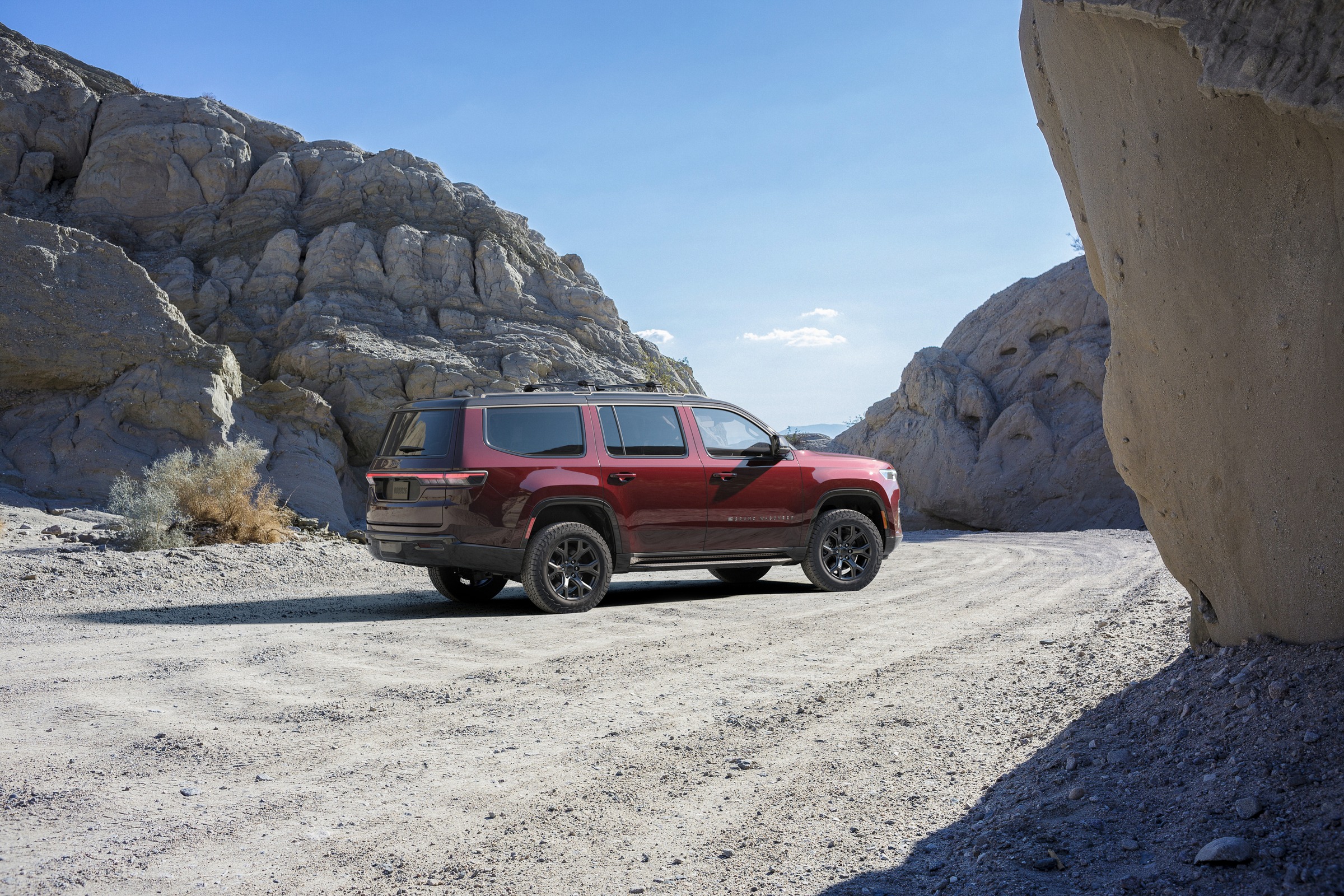 dark red Jeep Grand Wagoneer rear three quarter view on a canyon road
