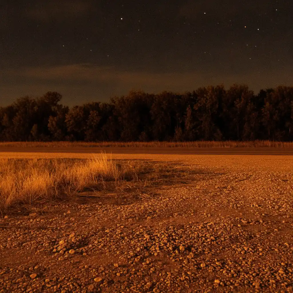 empty gravel shoulder beside a rural prairie road at night under a faint amber glow