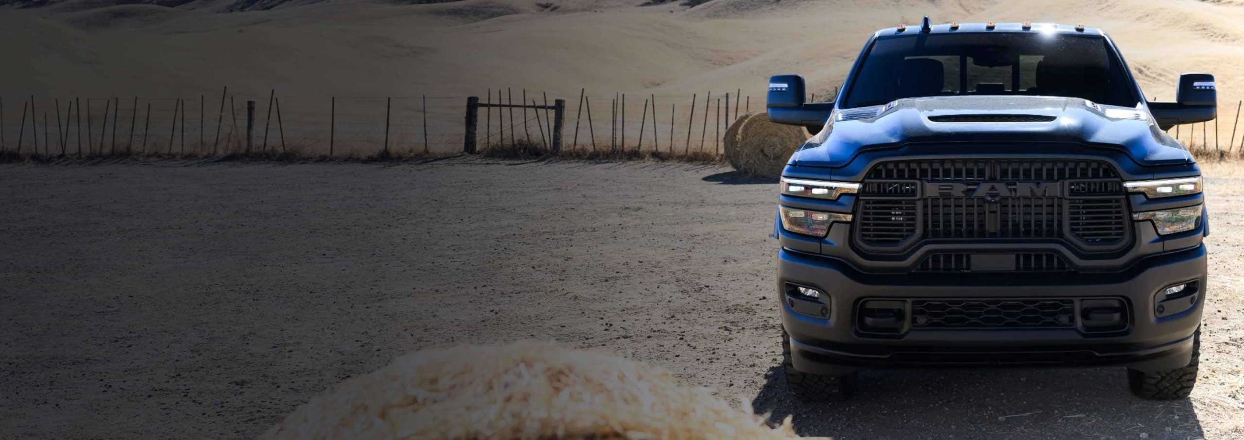 2026 Ram 2500 crew cab in dark blue on a farm lane with hay bales behind