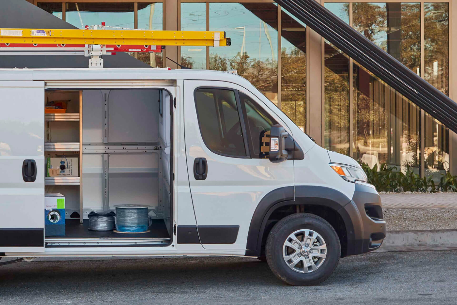 white Ram ProMaster with the sliding side door open showing shelving, wire spools and roof ladders