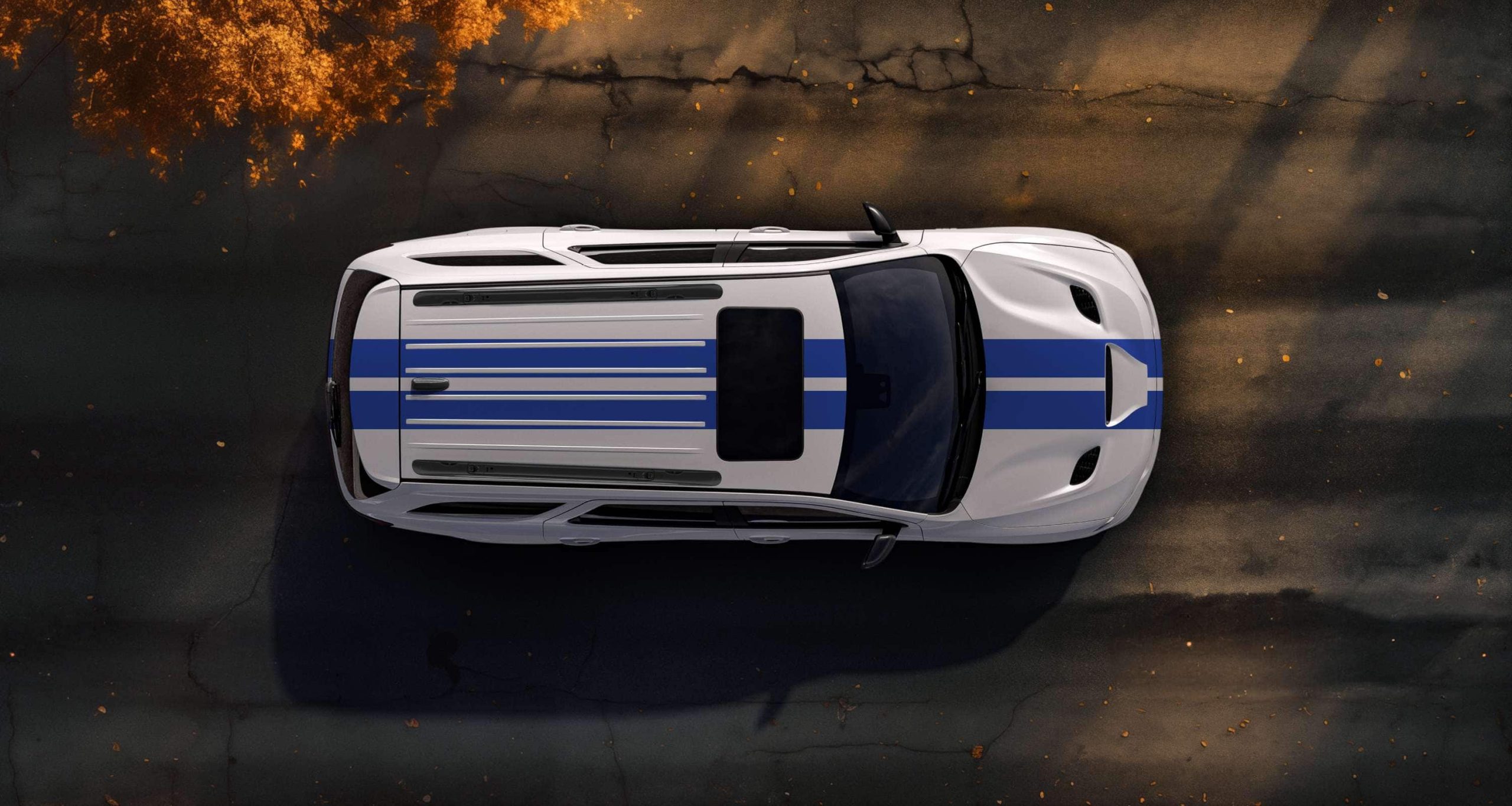Overhead view of a white Dodge Durango with blue dual stripes on pavement scattered with autumn leaves