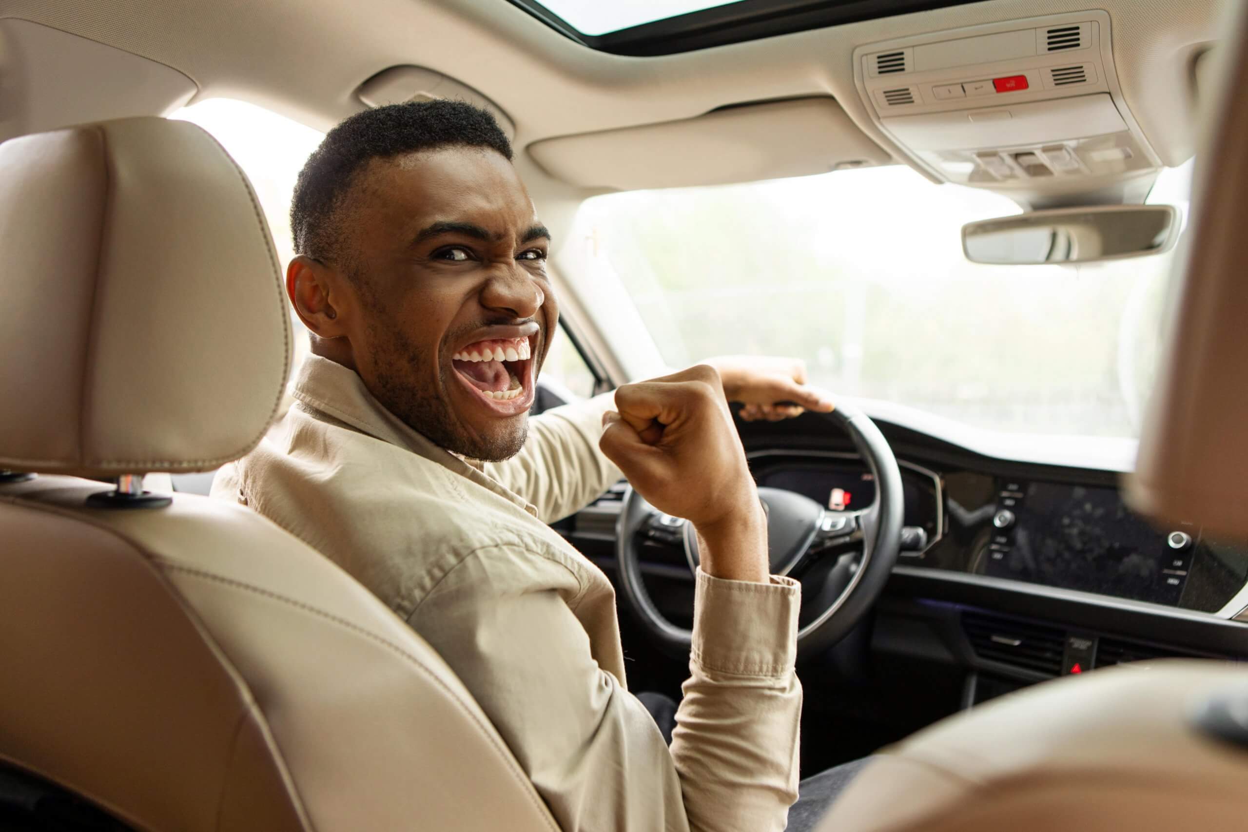 Young man who bought his first car and is smiling enthusiastically in the front seat